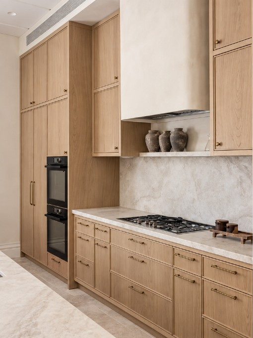 Warm oak kitchen cabinetry with a stone splashback, gas cooktop, built-in ovens and brass handles